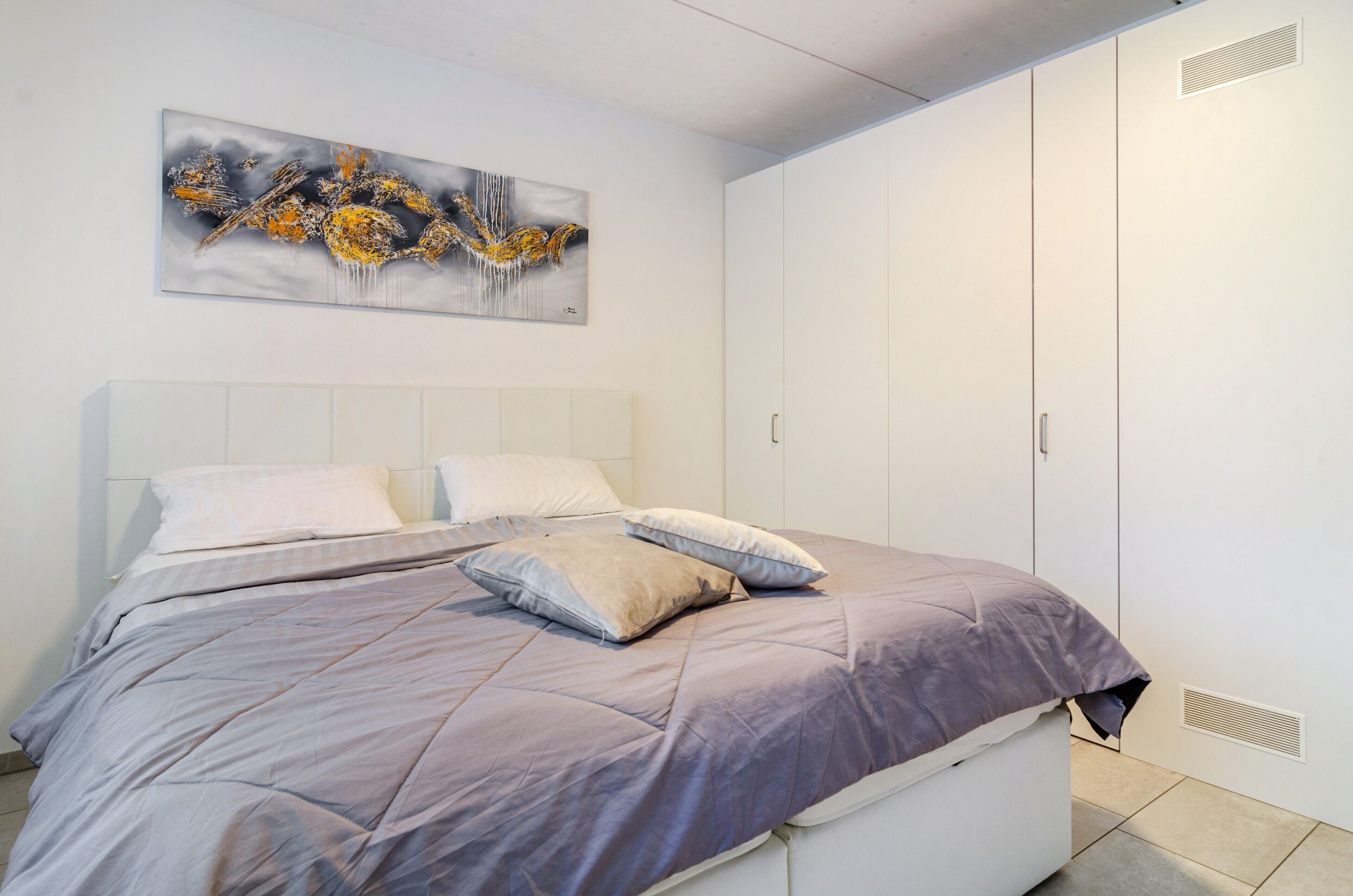 Un dormitorio con cama, almohadas, cabecera, una obra de arte en la pared y un armario.