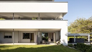 Un edifici modern de diversos pisos amb teulada plana, finestres grans i zona d'estar exterior coberta.