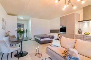 A modern bedroom with a bed, a sofa, a dining table, and a kitchen area.