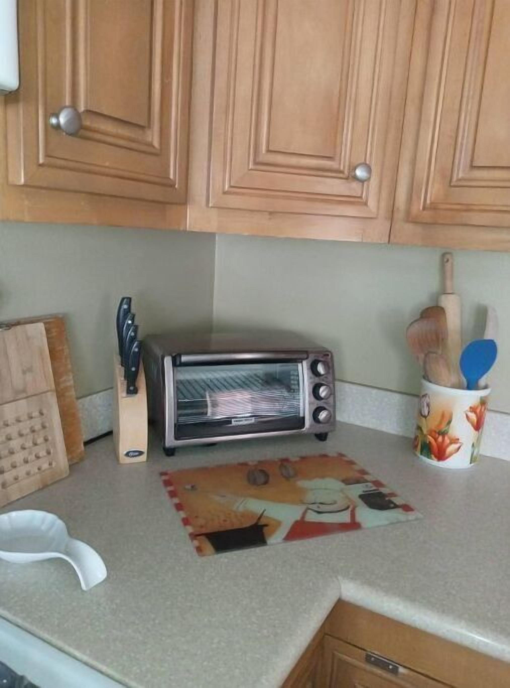 A kitchen with wooden cabinets, a toaster oven, a knife block, and a cup with wooden utensils.