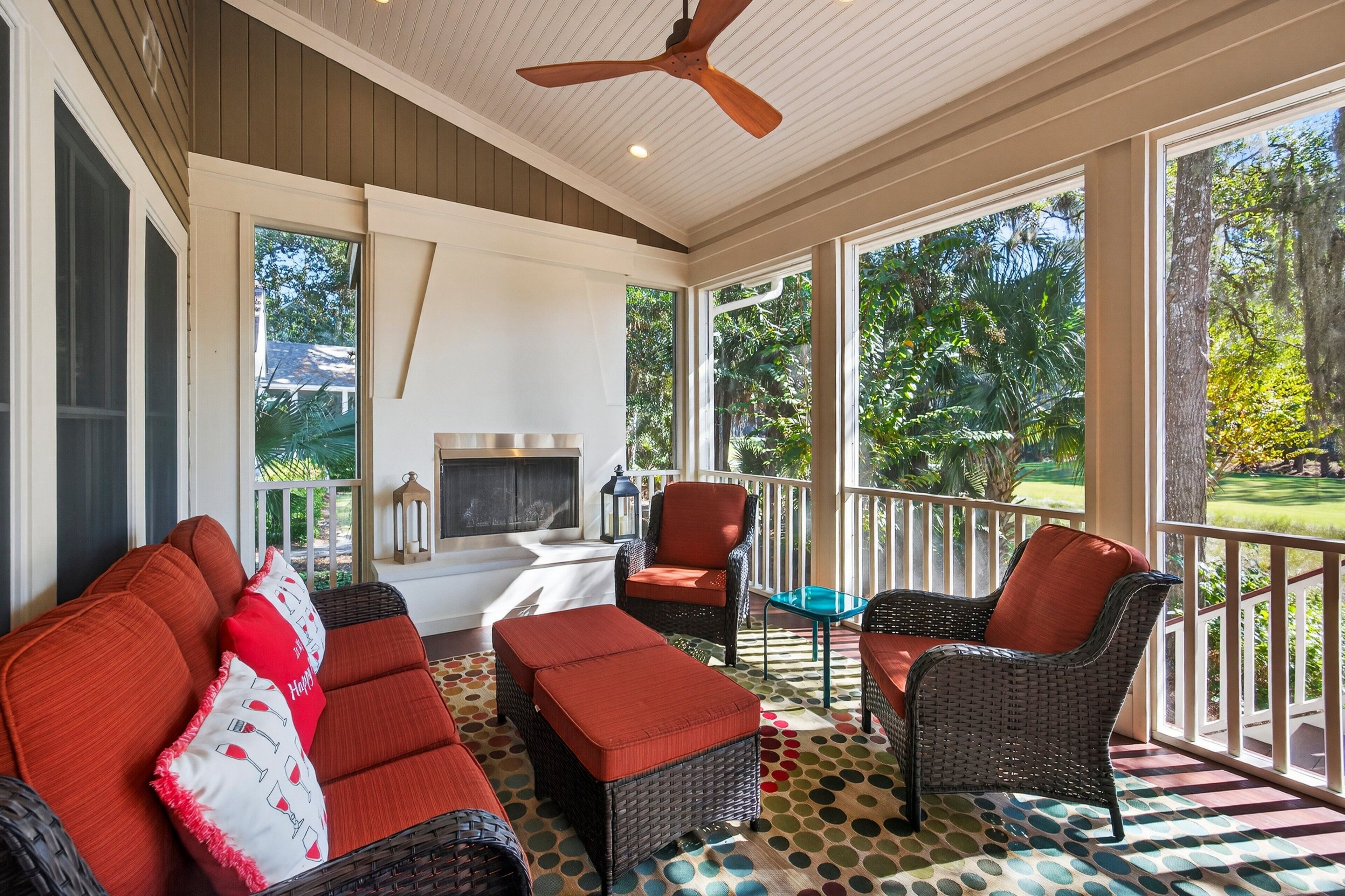 A covered outdoor seating area with wicker furniture, a ceiling fan, and large windows offering a view of the outdoors.