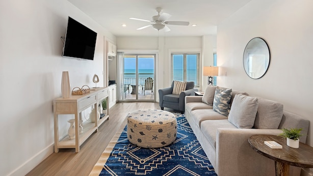 A modern living room with a flat-screen TV, a ceiling fan, a sofa, a coffee table, and a view to the outside. - BEACHFRONT! Modern, upgraded villa! East Beach Kiawah! (Kiawah Island)