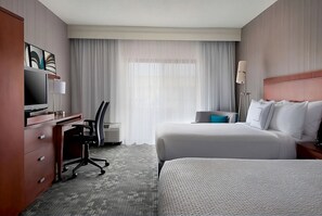 A hotel room with a bed, a desk, a chair, a TV, and a window with curtains.