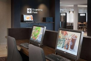 Un moderno vestíbulo de hotel con un cartel que dice 'Boarding Pass', una zona de estar con una mesa de comedor y dos monitores Dell mostrando imágenes de comida y bebidas.
