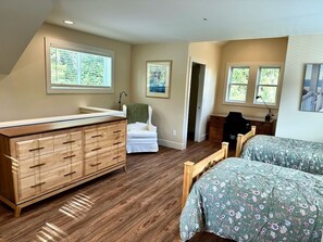 Un dormitorio con cómoda de madera, dos camas con ropa de cama floral, una silla y una ventana con persianas.