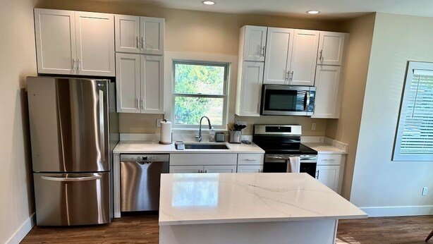 A modern kitchen with white cabinets, stainless steel appliances, and a marble countertop. - Cottage by the Trees (Bellingham)