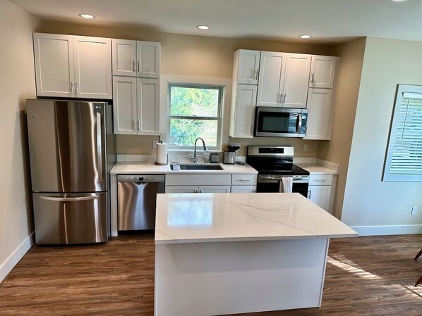 A modern kitchen with white cabinets, stainless steel appliances, and a marble countertop.