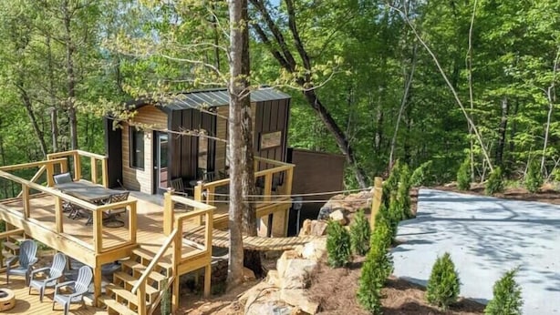 A cabin with a wooden deck and outdoor seating, surrounded by trees and a rocky landscape.