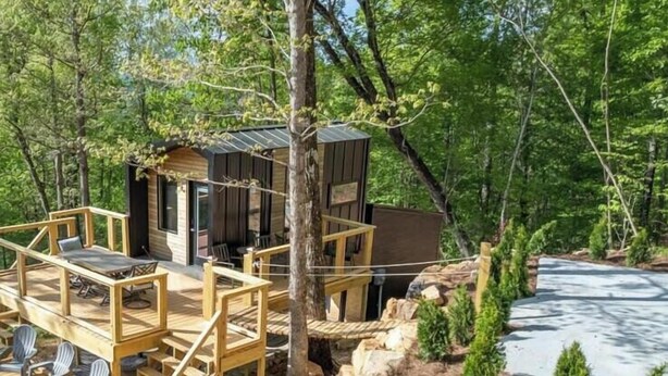 A cabin with a wooden deck and outdoor seating, surrounded by trees and a rocky landscape.