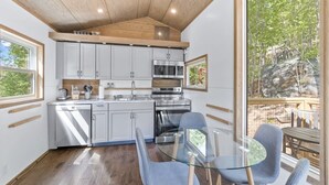 A modern kitchen with white cabinets, stainless steel appliances, and a glass dining table with blue chairs.