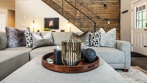 Een moderne woonkamer met een grijze bank, een houten salontafel en een trap met een houten wand.