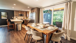 Een moderne keuken met houten kasten, roestvrijstalen apparatuur en een eethoek met een houten tafel voor vier personen.