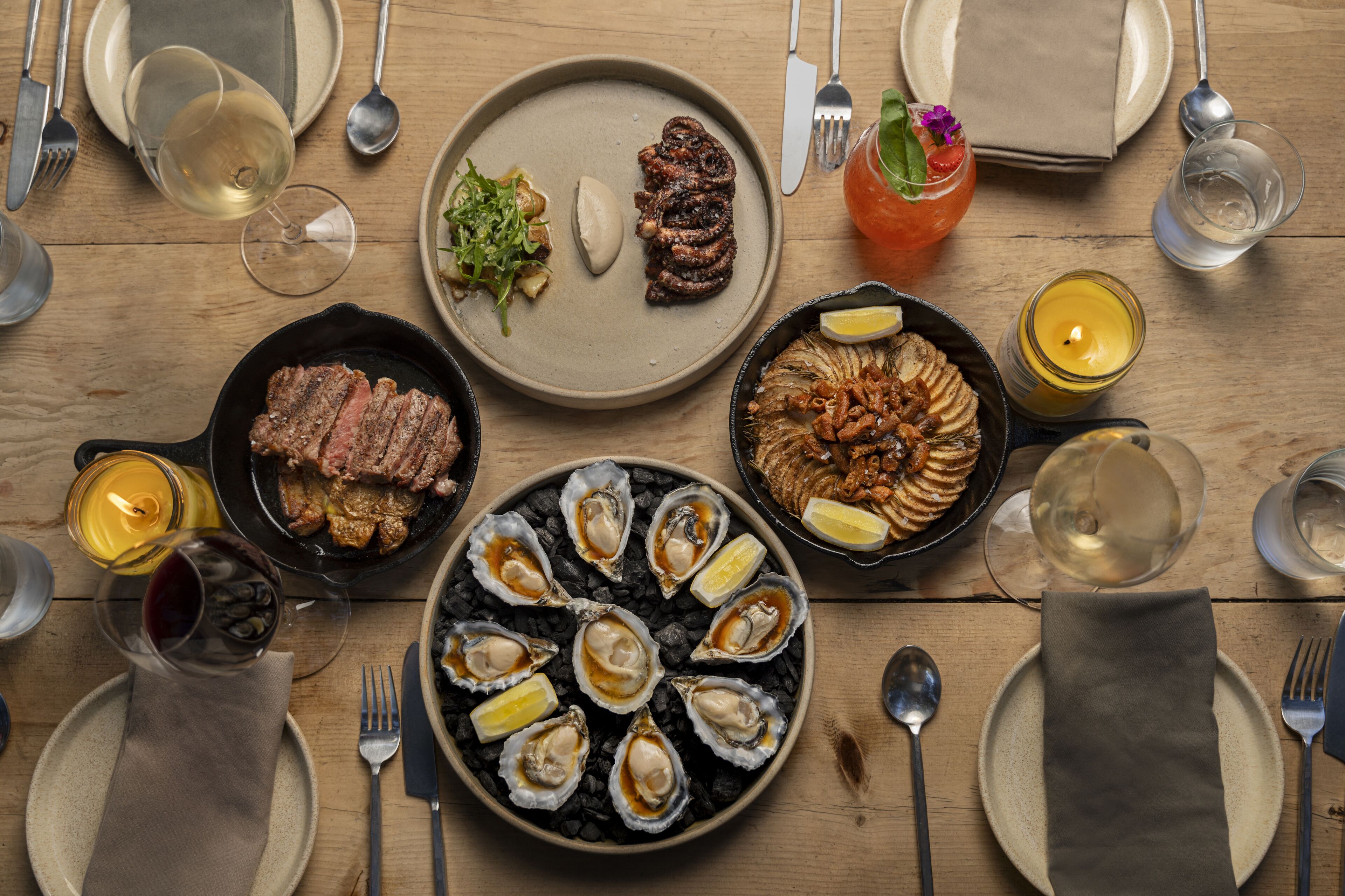 A wooden dining table set with plates of food, glasses of wine, and candles.
