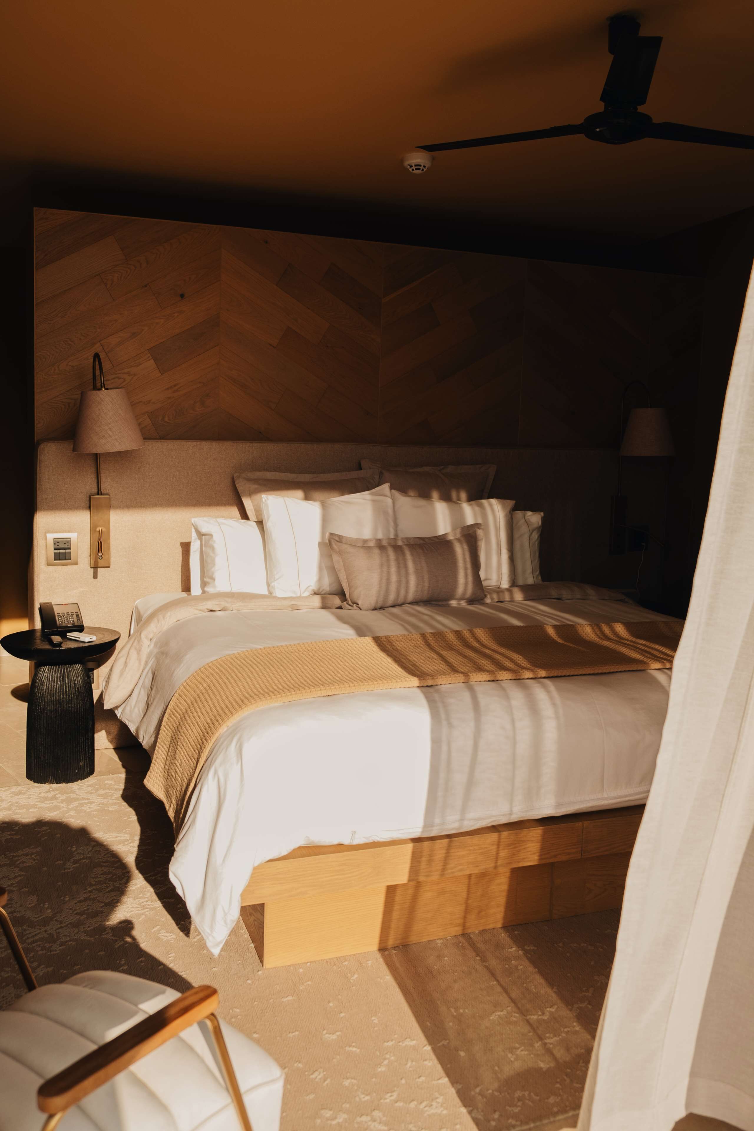 Een slaapkamer met een bed, nachtlampjes, een telefoon en een plafondventilator.