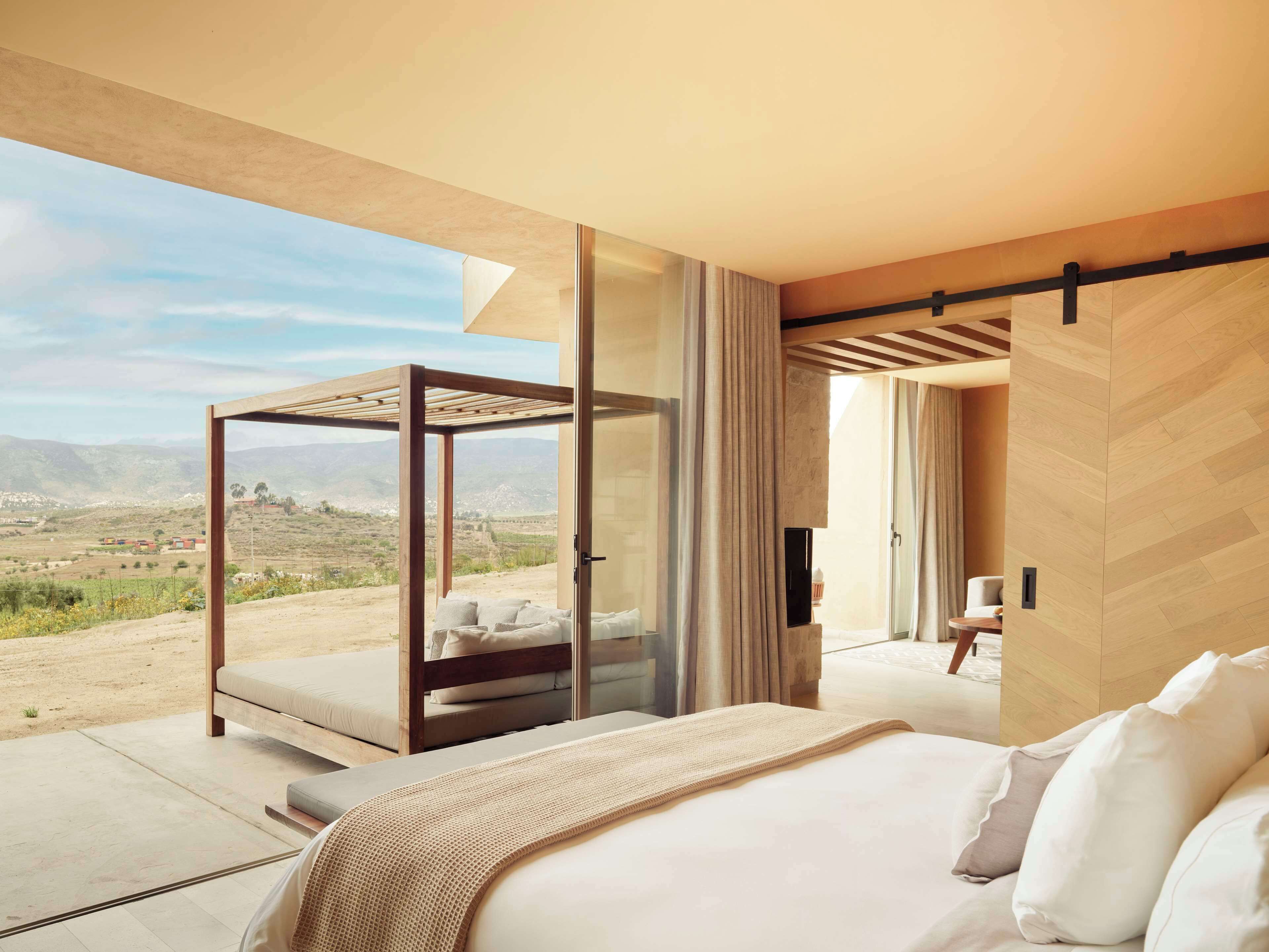 Un dormitorio moderno con una cama grande, un balcón con paredes de cristal y vistas al campo.