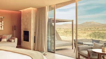 A modern bedroom with a large bed, a TV, and a view of a desert landscape through a sliding glass door.