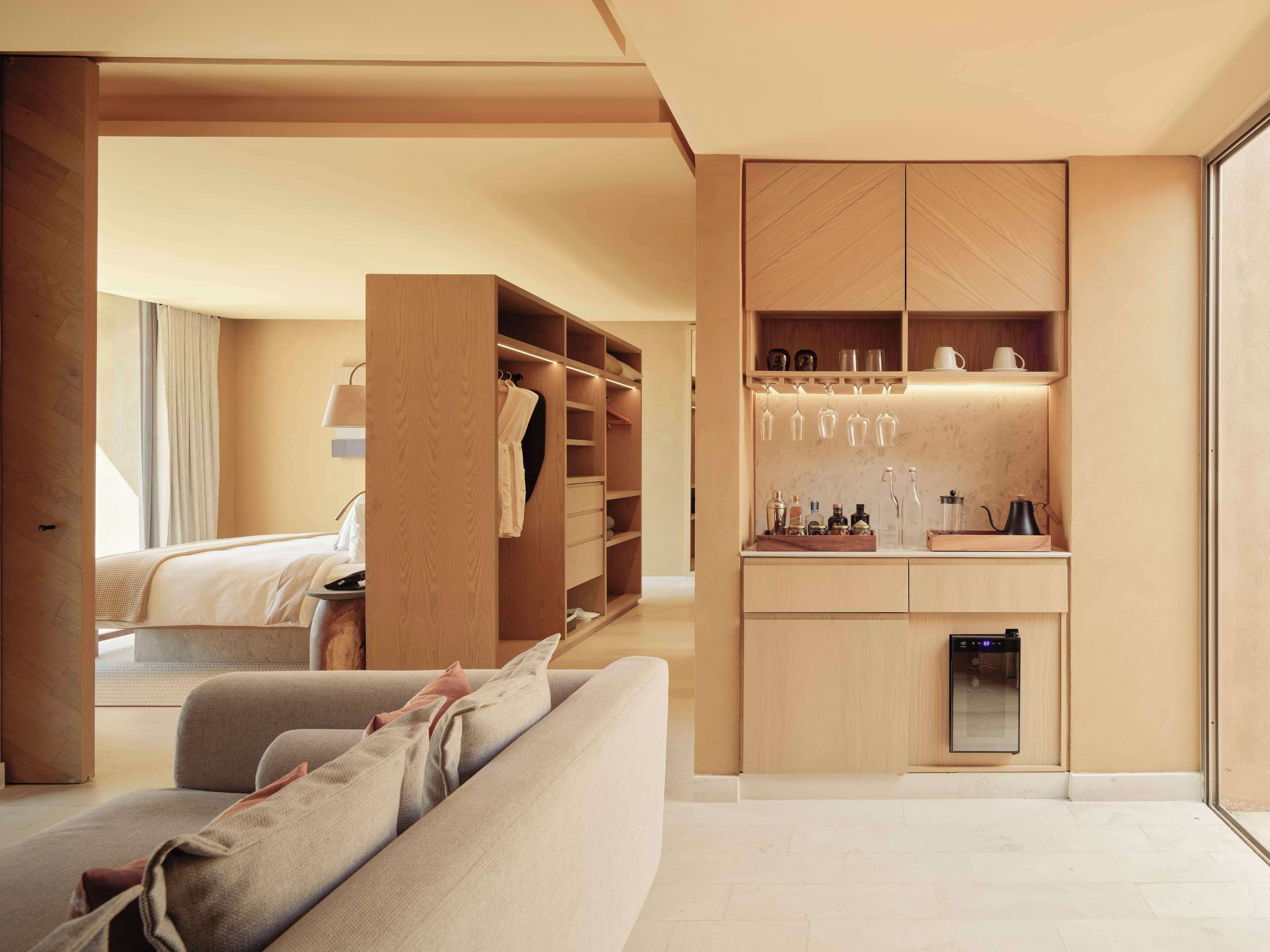 A modern hotel room with a built-in wardrobe, a kitchenette, and a seating area.