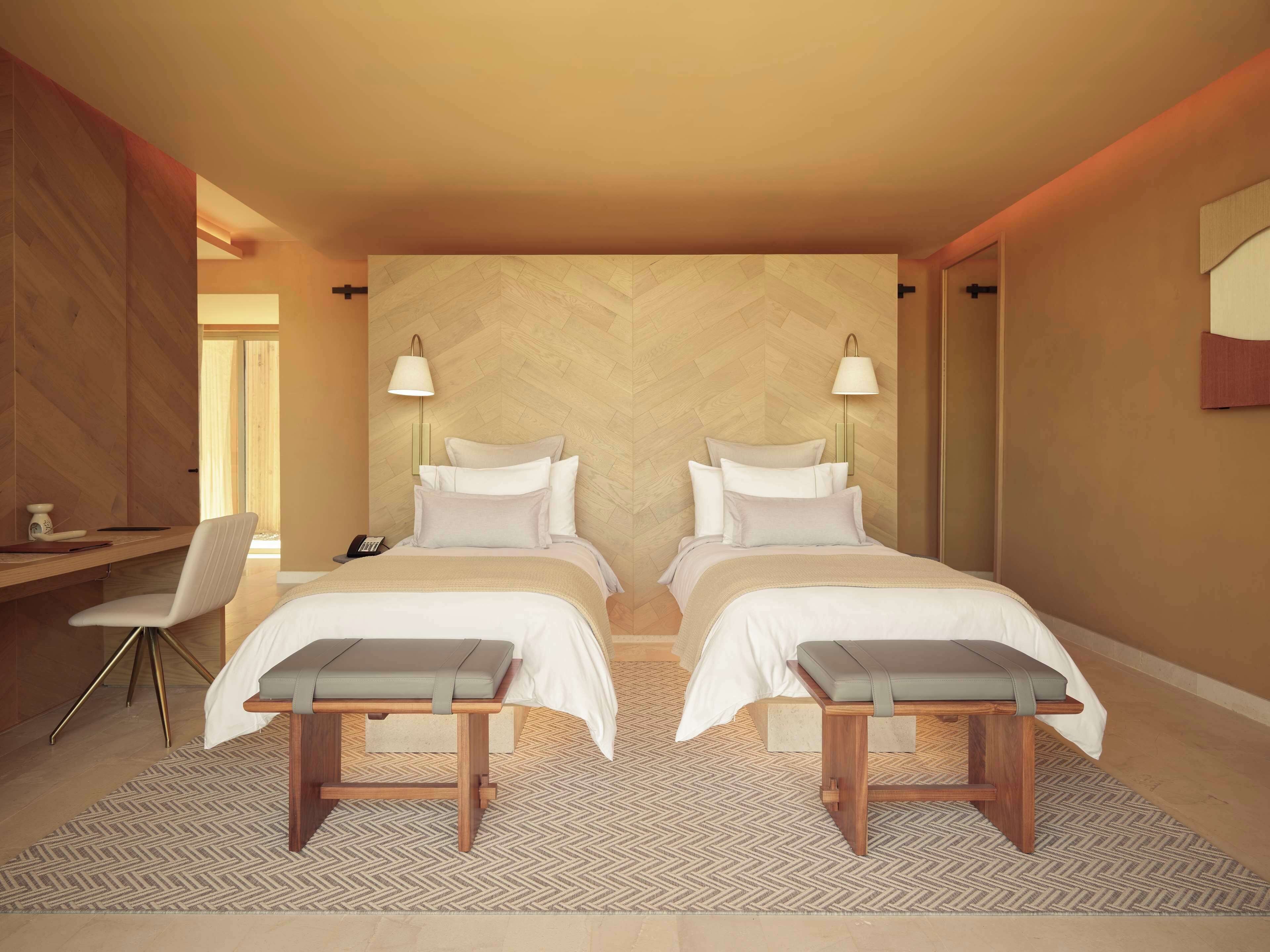 A modern hotel room with two beds, a desk, and a chair.