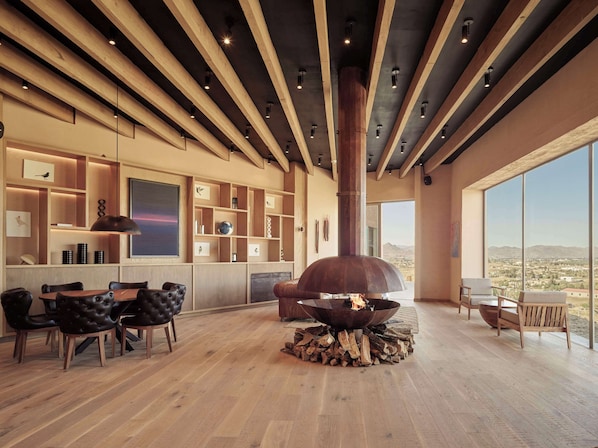 A modern interior with a fireplace, wooden beams, and a large window offering a view of the landscape. - Banyan Tree Veya Valle De Guadalupe (Valle de Guadalupe)