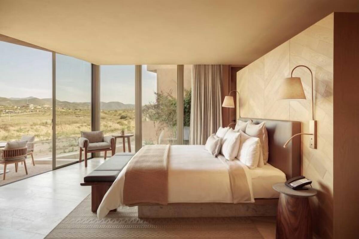 Un dormitorio moderno con una cama grande, una mesita de noche, una lámpara y vistas al paisaje desértico.