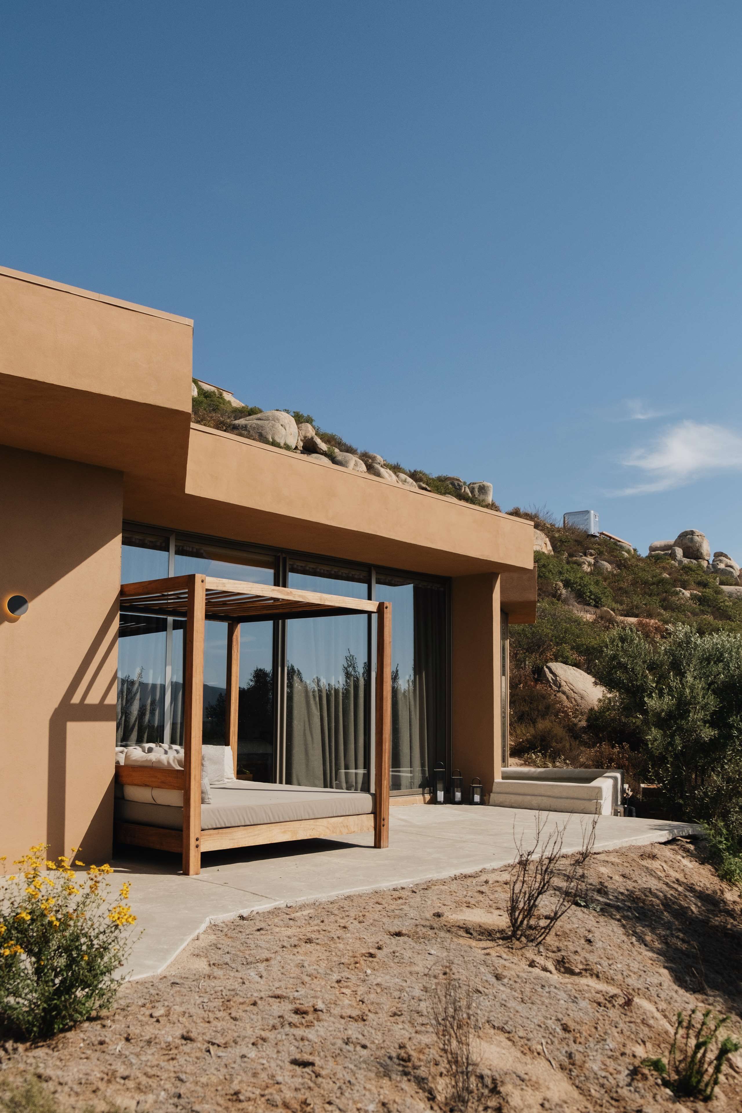 A modern house with a large glass window, a wooden bench, and a view of the surrounding landscape.