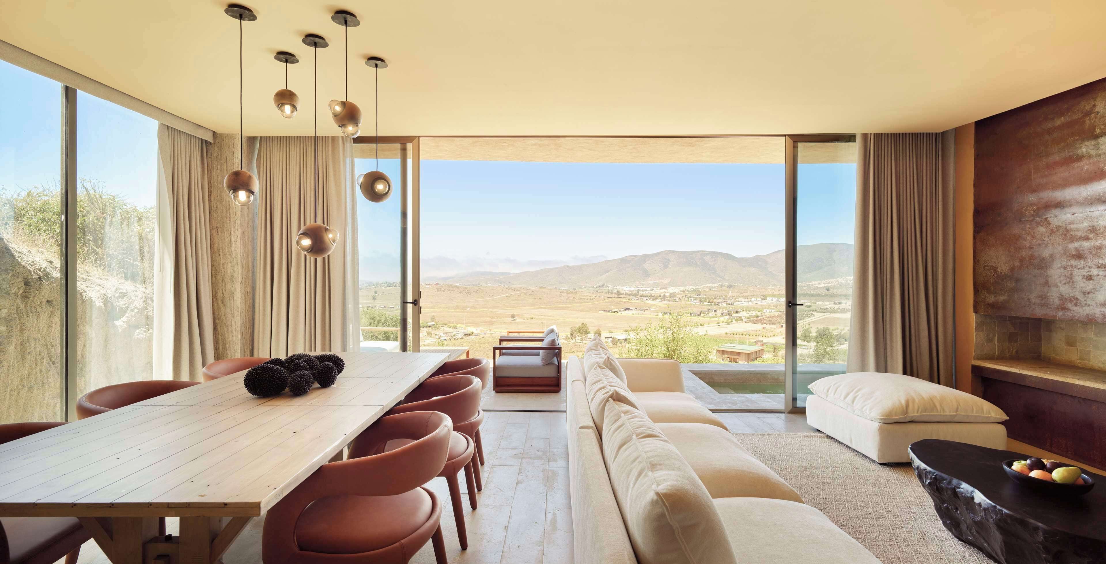 Un interior moderno con comedor, asientos y un amplio ventanal con vistas al campo.