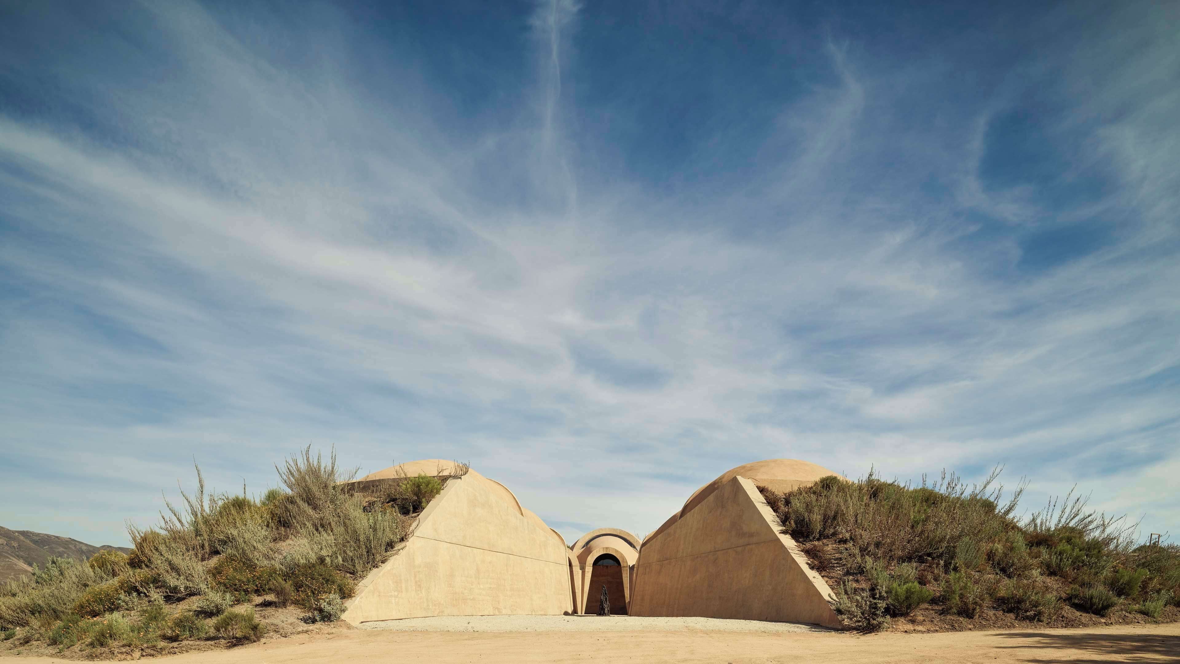 A desert landscape with a large, arched entrance leading into a structure with two dome-like buildings.