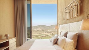 A modern bedroom with a large bed, a nightstand, a lamp, and a view of a landscape through a large window. - Banyan Tree Veya Valle De Guadalupe (Valle de Guadalupe)