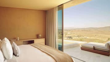 A bedroom with a large bed, a bedside table, a lamp, and a view of a landscape through a glass door.