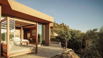 A modern outdoor bedroom with a bed, seating area, and a view of the surrounding landscape.