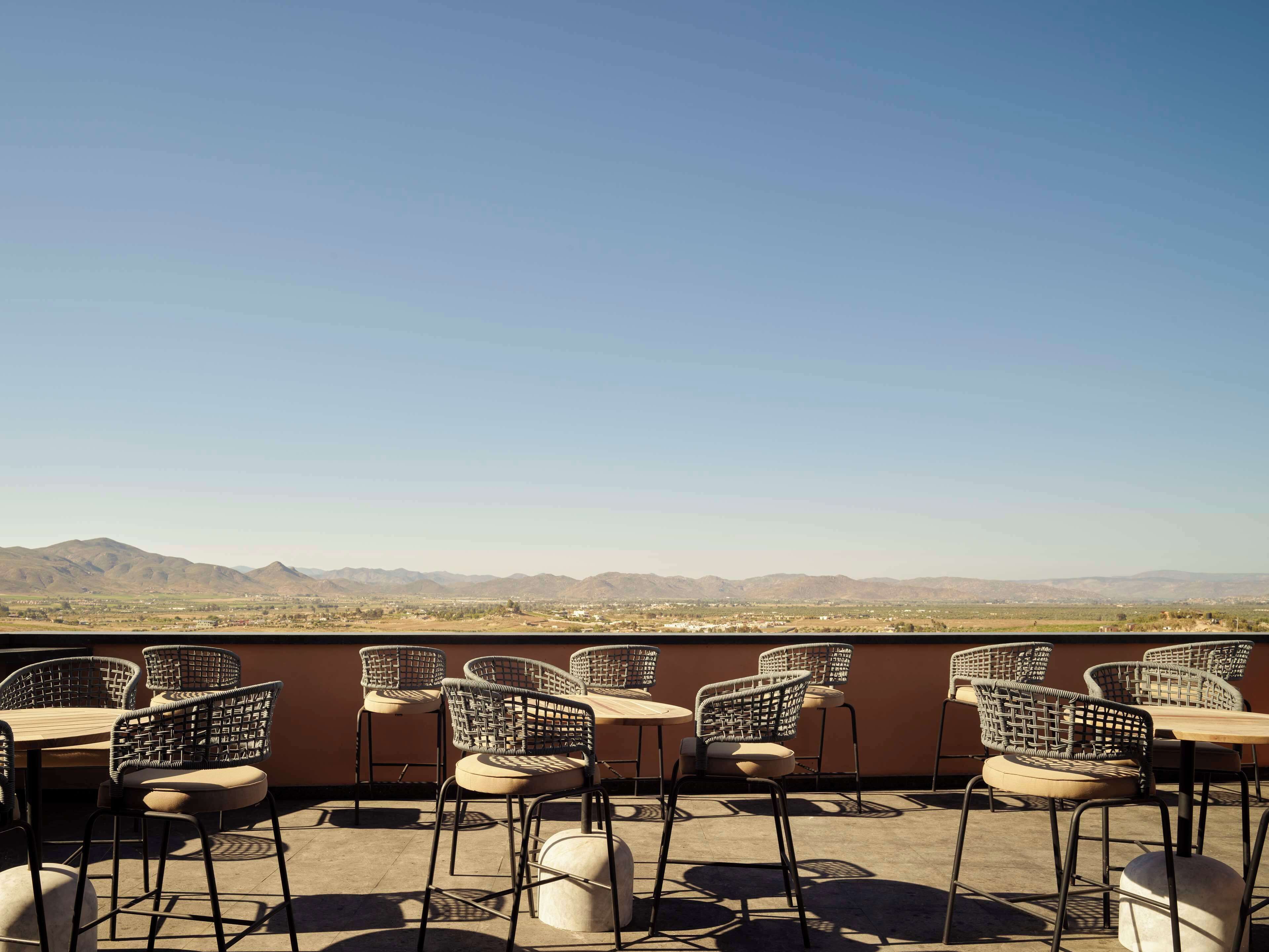 Un espacio de estar al aire libre con sillas y mesas de mimbre, con vistas a un paisaje montañoso.