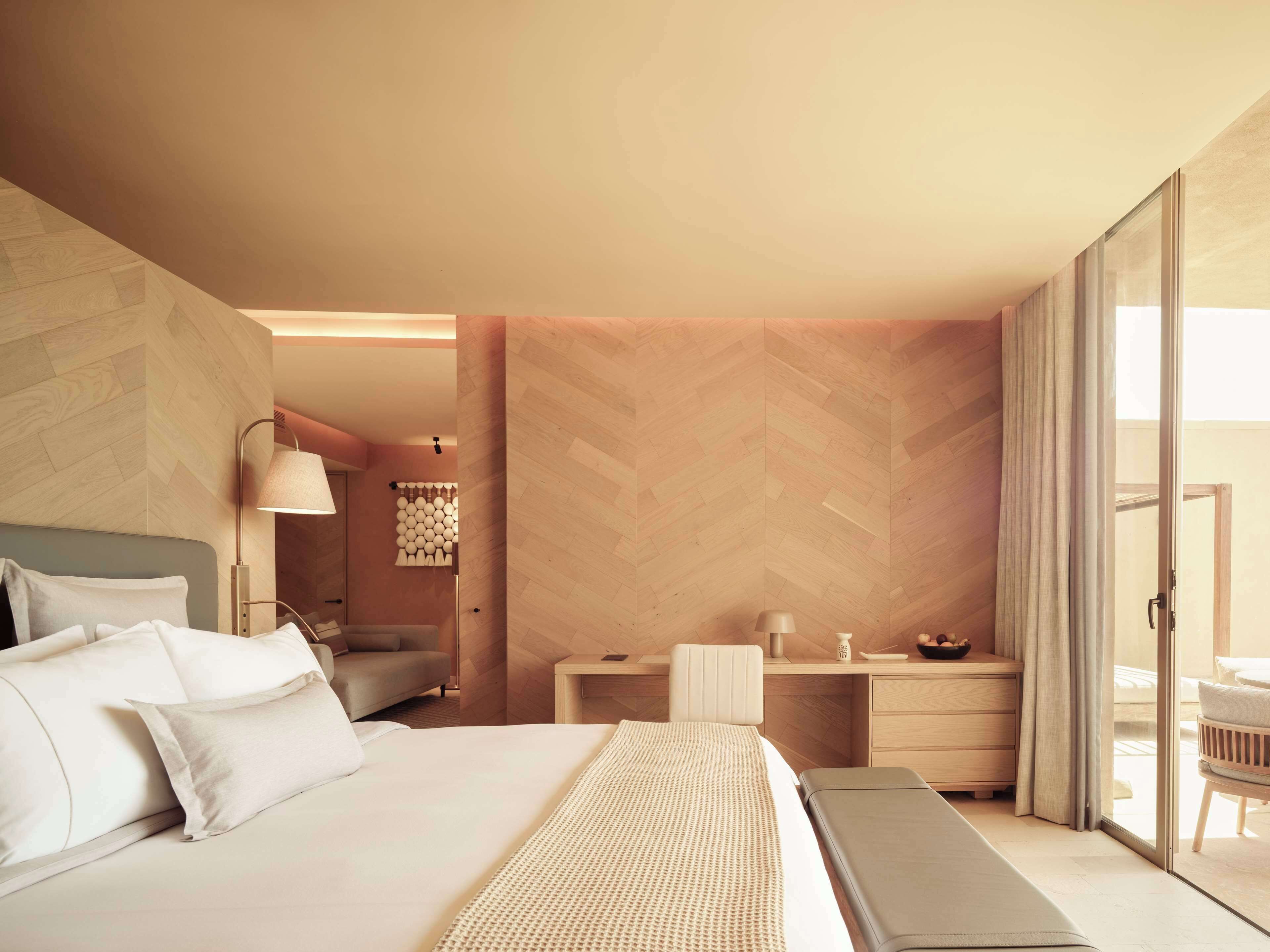 A modern hotel room with a large bed, a desk, and a view of the outdoors.
