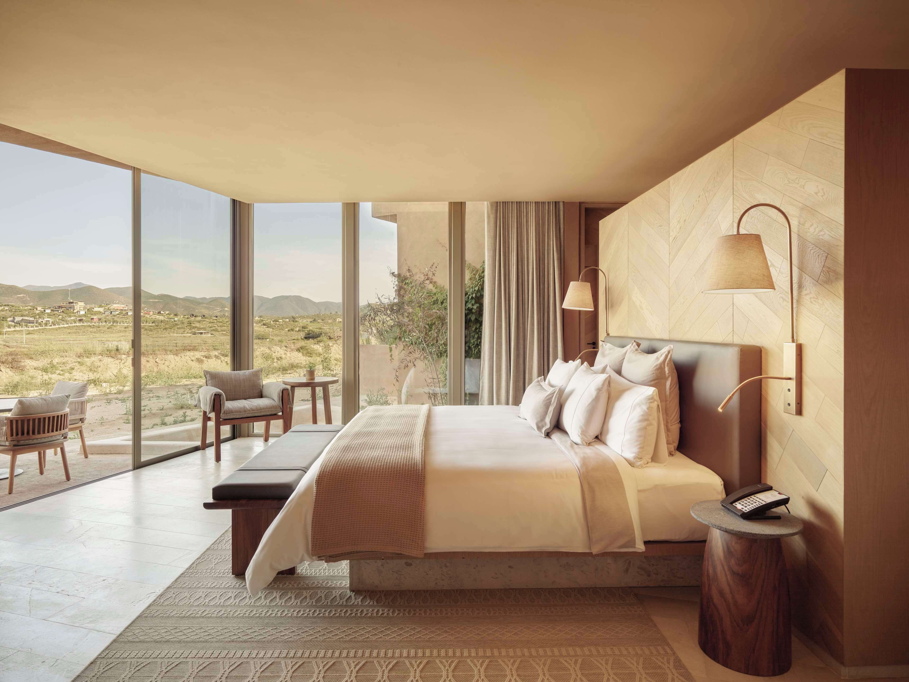 A modern bedroom with a large bed, a desk, and a view of the countryside.
