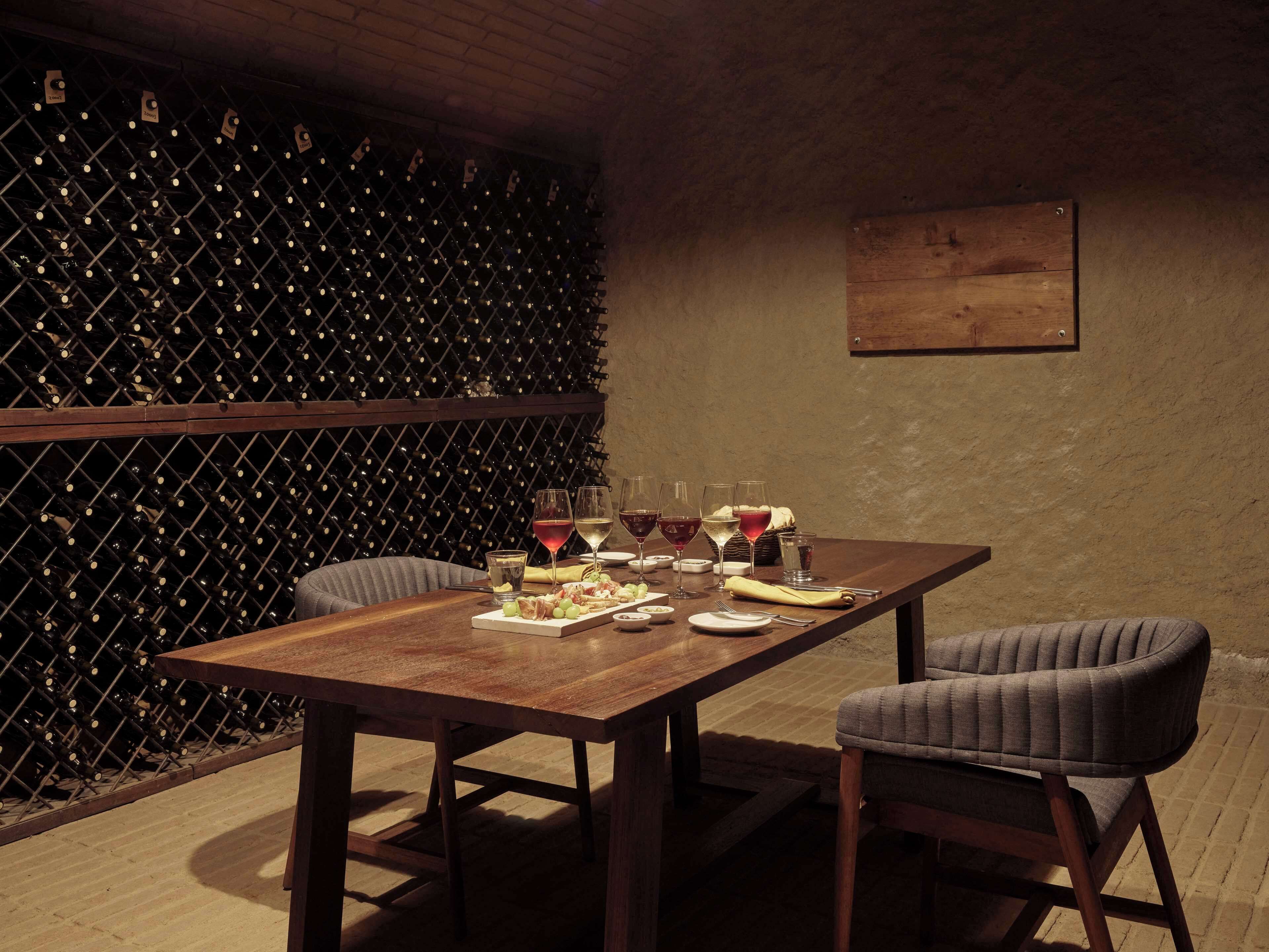 Un comedor con una mesa de madera, dos sillas tapizadas y una estantería para vinos al fondo.