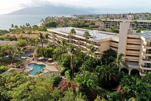 Un hotel con diversi piani, una piscina e rigogliosa vegetazione.