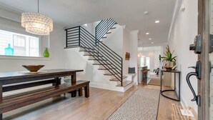A modern interior with a staircase, wooden flooring, a dining area with a bench, and a patterned rug. - 12 South Family Home With Den + Screened Porch     |     Walk to Shopping in 12 South, 10 Minutes to Broadway, Dedicated Parking, Perfect for Families, 24 Hr Hospitality (Nashville)