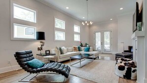 A spacious living room with a black leather chair, a white sofa, and a cowhide pouf. - 12 South Family Home With Den + Screened Porch     |     Walk to Shopping in 12 South, 10 Minutes to Broadway, Dedicated Parking, Perfect for Families, 24 Hr Hospitality (Nashville)