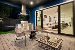 An outdoor patio with wicker furniture, a grill, and a dining table with drinks. - Stylish 7BR Austin Home | Heated Pool & Hot Tub (Austin)