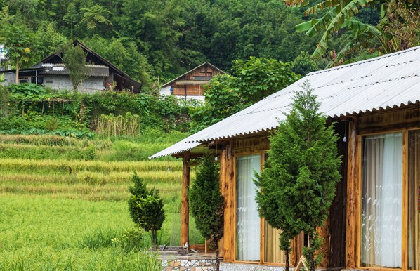 A rustic wooden house with a tiled porch, surrounded by lush greenery and rice fields. -  Hoa Chanh Bungalow (Sa Pa)