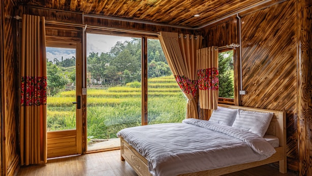 Une chambre avec un plafond en bois, un grand lit et une vue sur un paysage verdoyant par la fenêtre.