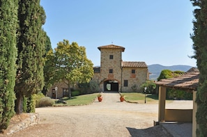 Un edificio in pietra con una torre, un vialetto sterrato e un cielo sereno.