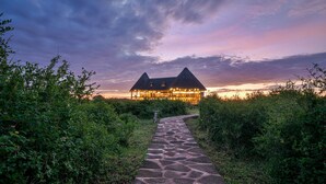 A thatched-roof building with a stone pathway leading to it, surrounded by greenery. - Aardvark Safari Lodge (Kasese)