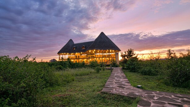 A large, open-air structure with multiple rooms, surrounded by lush greenery and a stone pathway leading to it. - Aardvark Safari Lodge (Kasese)