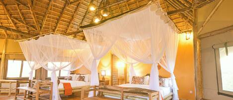 Habitación con dos camas bajo un tejado de paja, muebles de madera y un ventanal grande.