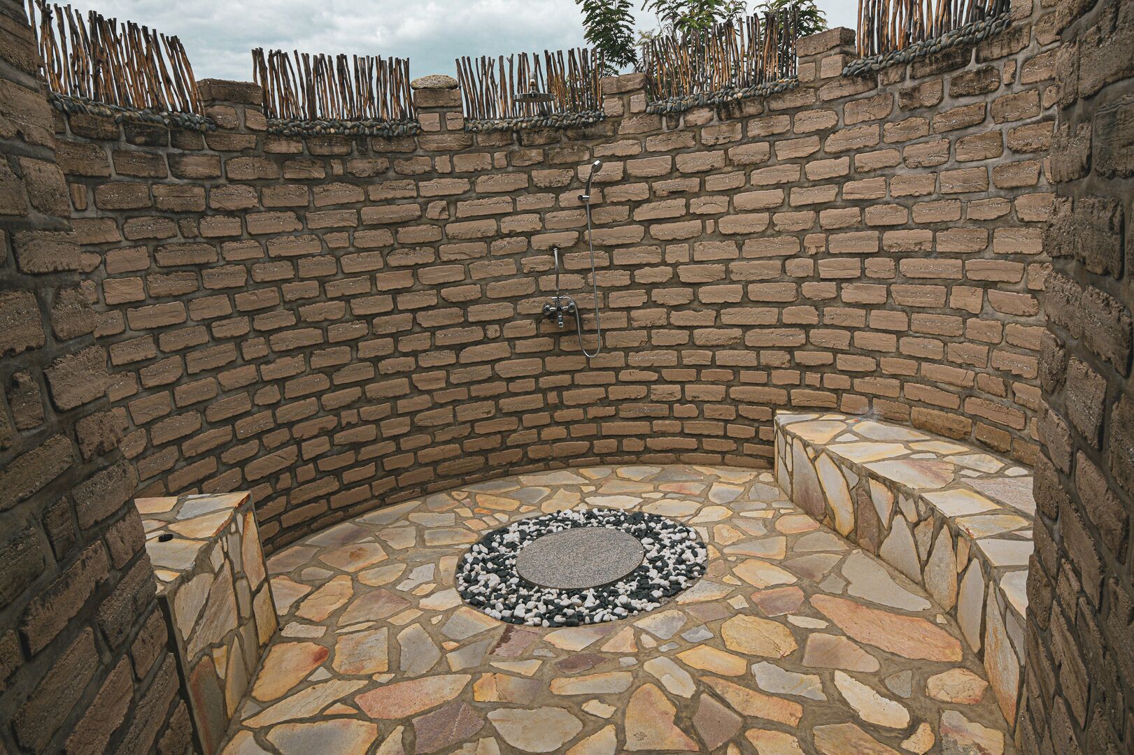 A stone-walled outdoor area with a circular stone floor and seating.