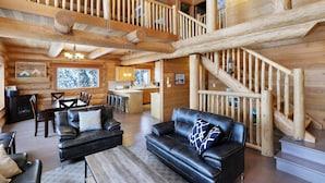 Interior espaçoso de uma cabana de madeira, com sala de estar, área de jantar, cozinha e escada.