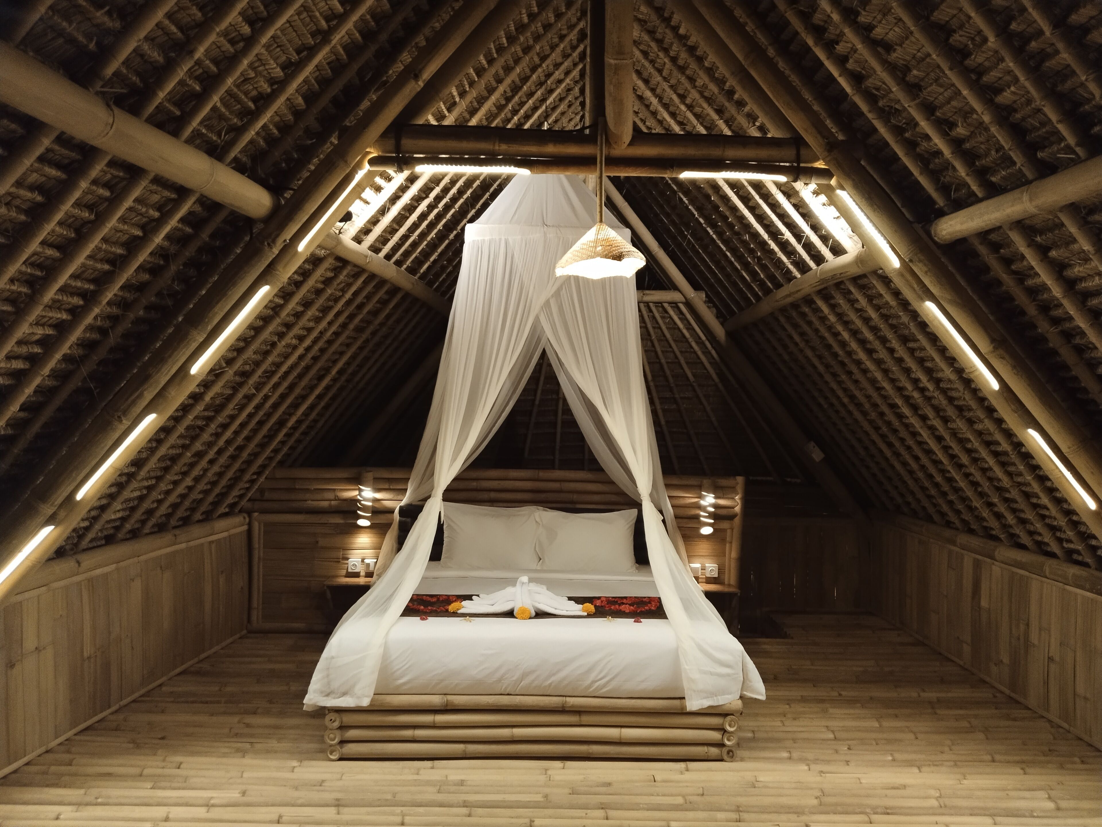 A high-ceilinged room with a bed under a canopy, wooden walls, and a sloped roof with exposed beams.