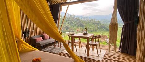 A room with a bed, a small table, and a view of the landscape.