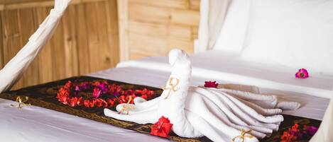 Una cama con una toalla blanca doblada en forma de cisne, rodeada de flores rojas y rosas, y una bandeja decorativa.