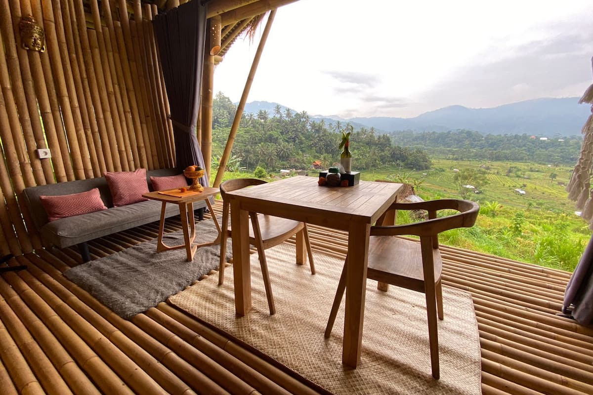A bamboo room with a sofa, table, and chairs, overlooking a lush landscape.